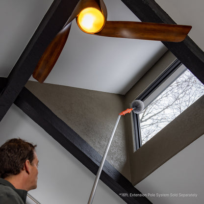 Motorized cobweb duster on extension pole cleaning interior window; extension pole sold separately.