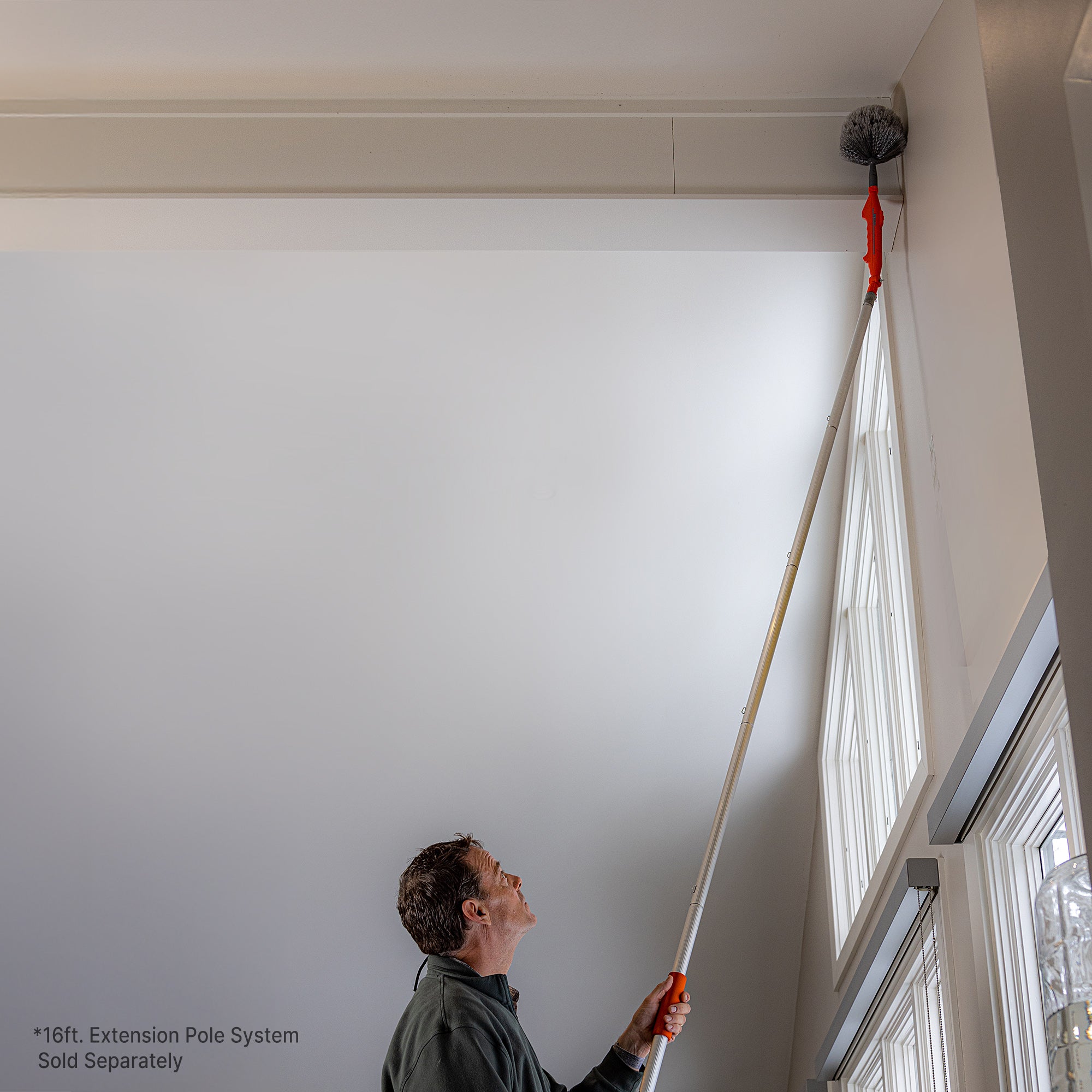 Motorized cobweb duster on extension pole cleaning corner in high ceiling; extension pole sold separately.